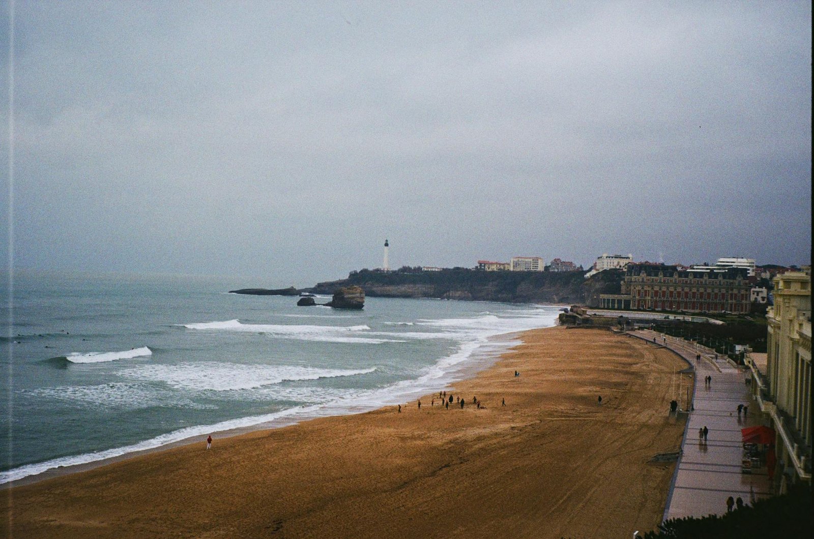 Beachfront and lighthouse at Biarritz with waves and cityscape in view.