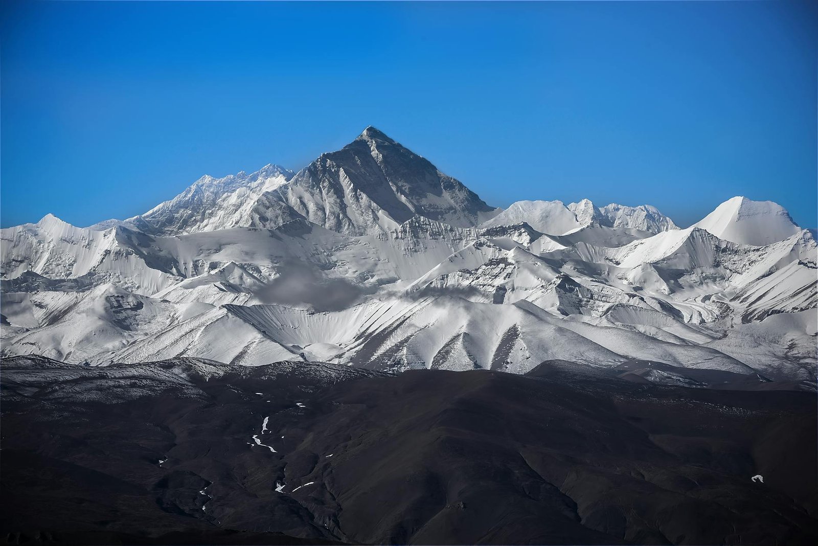 Stunning view of Mount Everest surrounded by snowy peaks under a clear blue sky.